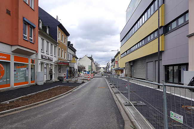 Blick in die baustellenbedingt gesperrte Schlossstraße in Neuwied mit frisch verlegten dunklen Pflastersteinen und Bauzäunen unter bewölktem Himmel.
