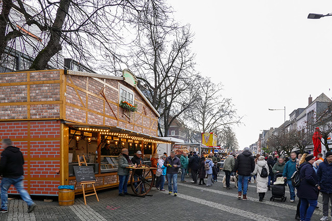 Eine rustikale Holzhütte mit Fachwerk-Optik dient als Verkaufsstand auf dem Festival. Besucher stehen davor und genießen ihre Speisen im Stehen. Foto: Elke Döbbeler