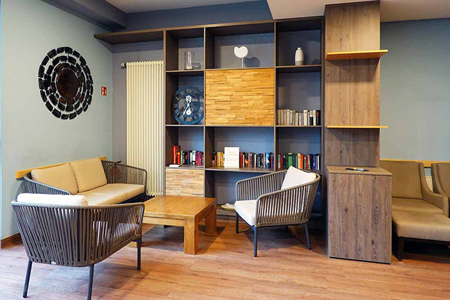 Einladender Aufenthaltsbereich mit grauen Loungesesseln, einem Holzcouchtisch und einem großen Wandregal voller Bücher.