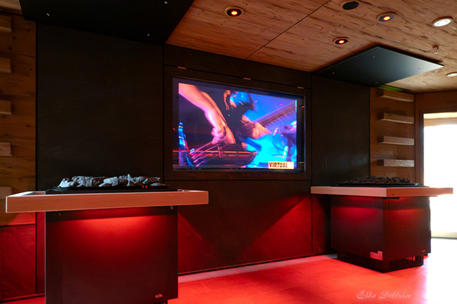 Nahaufnahme der Event-Technik in der Sauna: Ein Bildschirm zeigt eine dynamische Performance in leuchtendem Blau, während der Raum in tiefrotes Licht getaucht ist. Foto: Elke Döbbeler