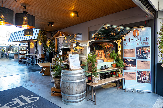 Ein gemütlicher, zu einer Kaffeebar umgebauter Kleintransporter („Ahrtaler Kaffeeröster“) in einem Innenhof. Dekoriert mit Lichterketten, Weinfässern und kleinen Tannenbäumen.